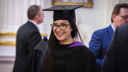 Woman smiling in a graduation gown in a hall 