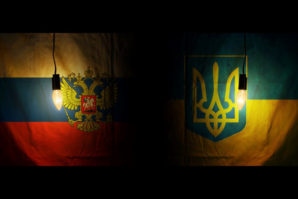 Russian and Ukranian flags hanging in a dark room illuminated by light bulb