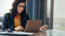 Woman sitting at a table, looking at a laptop and business records 